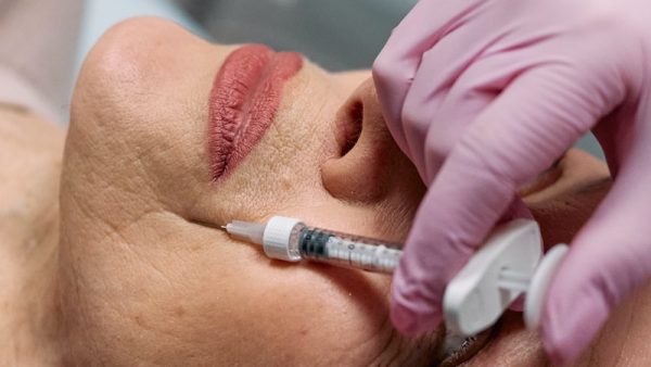 Hands Wearing Medical Gloves Injecting Syringe on Client's Face