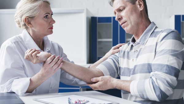 A female doctor in a white coat examines a man's painful arm in a medical office