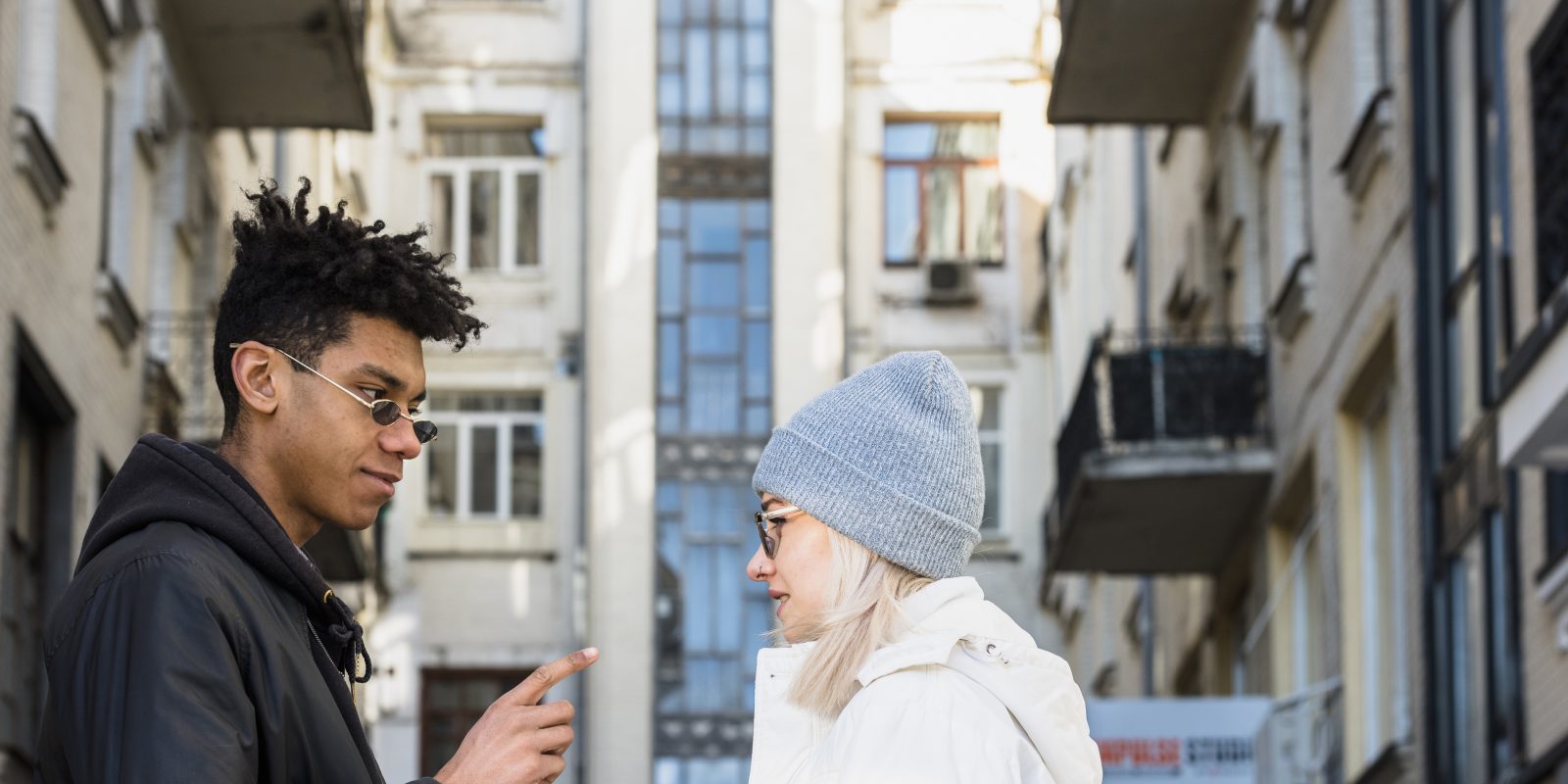 Young man pointing during conversation with woman in urban apartment courtyard between residential buildings modern