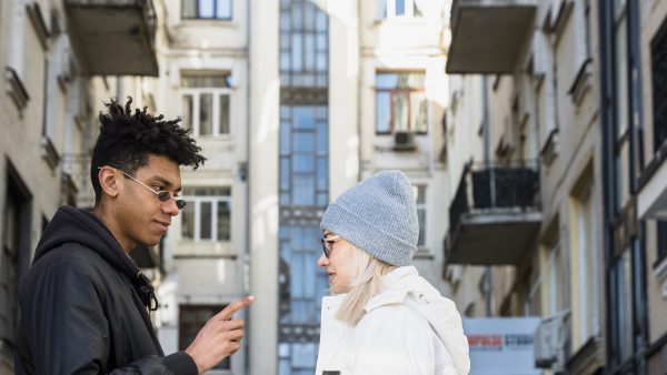 Young man pointing during conversation with woman in urban apartment courtyard between residential buildings modern