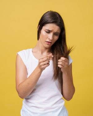 A woman holds her hair up, examining it closely with a thoughtful expression on her face