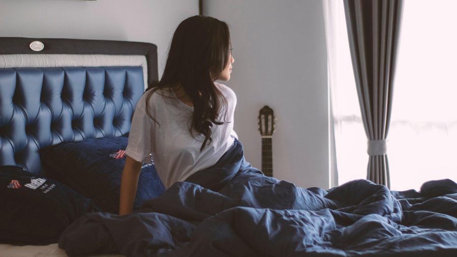 A woman sitting on the bed wearing grey top