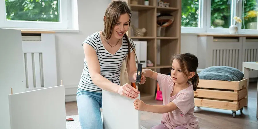 A woman and a child are assembling a white cabinet together, focused on their task