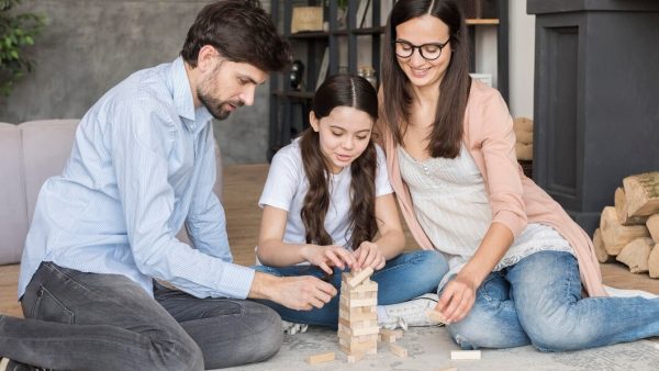 A family joyfully playing together, building structures with colorful wooden blocks on a bright, sunny day