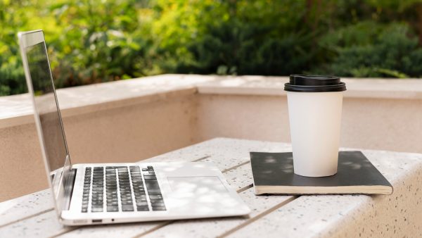 A laptop alongside a steaming cup of coffee rests on a table, suggesting a productive work environment