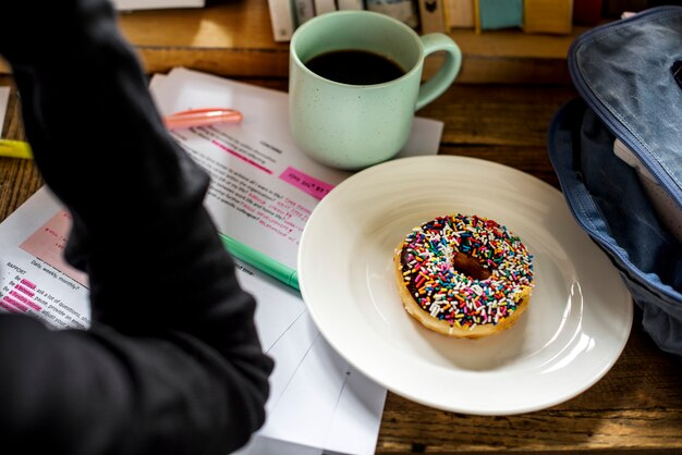 Coffee and sprinkled doughnut on a desk with documents for a perfect study snack in a cosy workspace